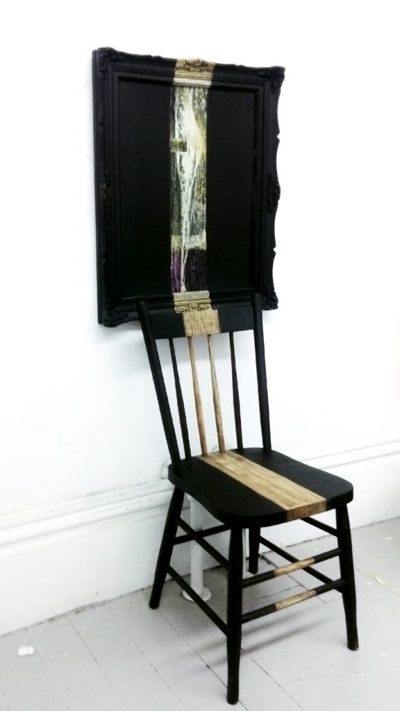 Hung painting with frame painted black, one line of colour runs down the face of the painting on to a chair.